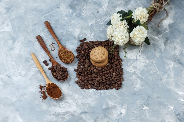 Flat lay cookies with coffee beans, instant coffee, coffee flour in wooden spoons, flowers on light blue marble background. horizontal