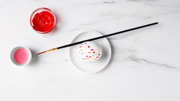 Flat lay of decorated easter egg on plate with paint and paintbrush