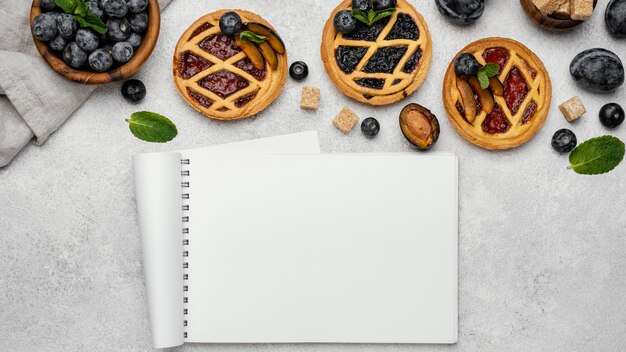 Flat lay of delicious fruit pies with notebook