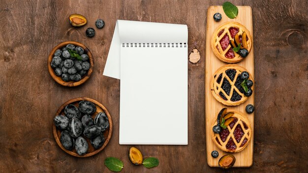 Flat lay of delicious fruit pies with plums and notebook