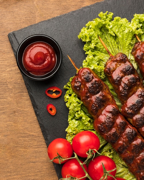Flat lay of delicious kebab on slate with ketchup and salad