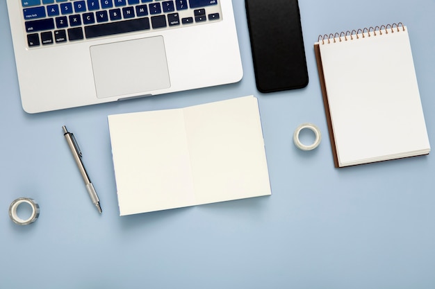 Flat lay desk arrangement with empty notepad on blue background