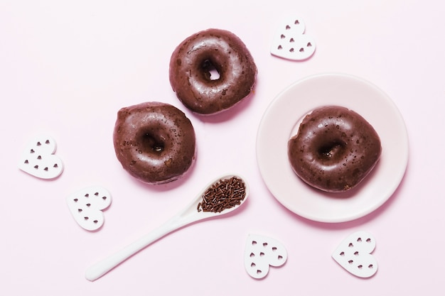 Free photo flat lay donuts with paper hearts on pink background