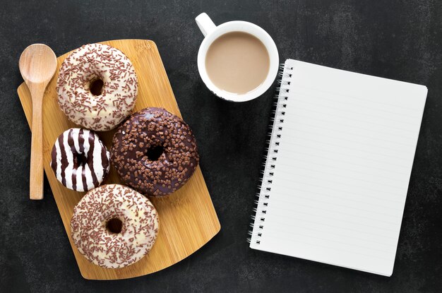 Плоские лежат пончики на разделочную доску с ноутбуком и кофе
