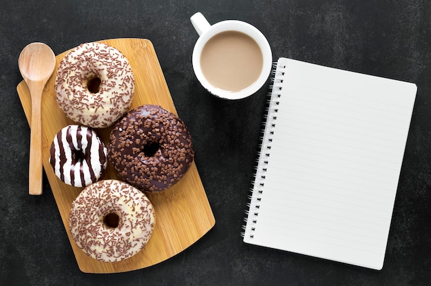 Flat lay of doughnuts on chopping board with notebook and coffee