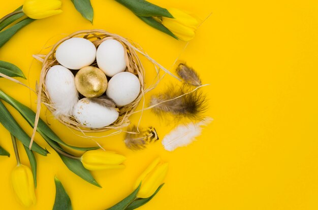 Flat lay of easter eggs in basket with tulips and feathers
