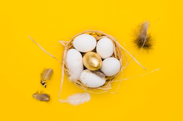 Flat lay of eggs in basket for easter with gold paint and feathers