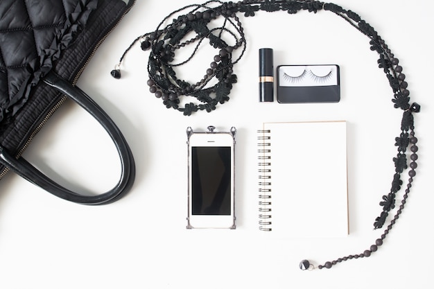 흰색 배경에 고립 된 검은 개념, 평면도, 빈 노트북, 핸드폰 및 여자의 액세서리의 평면 배치