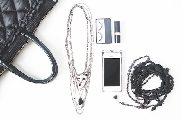 Flat lay of empty notebook, cellphone and woman's accessories in black concept, top view, isolated on white background