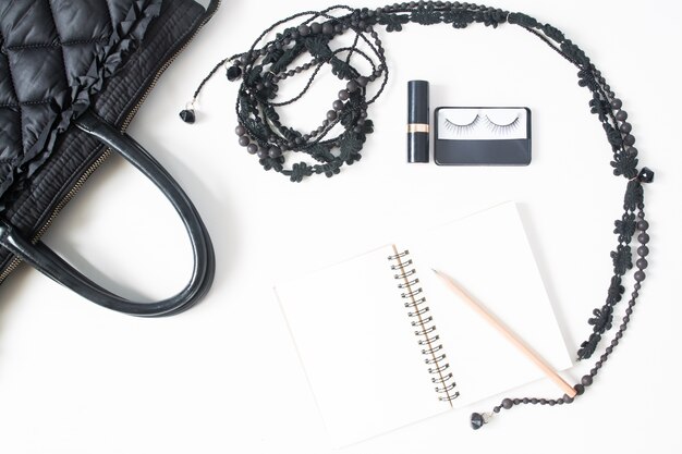 Flat lay of empty notebook, pencil and woman's accessories in black concept, top view, isolated on white background