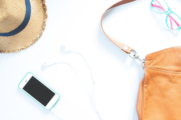 Flat lay female accessories collage with hat, bag, fashion glasses, mobile phone and earphone on white background.