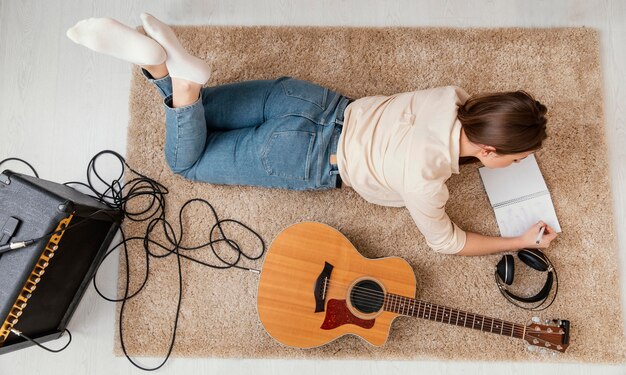 Flat lay of female musician at home writing song with headphones and acoustic guitar