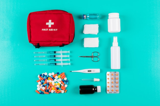 Foto gratuita kit di pronto soccorso disteso con pillole, termometro, spray, pillole e benda su sfondo blu ciano. orizzontale