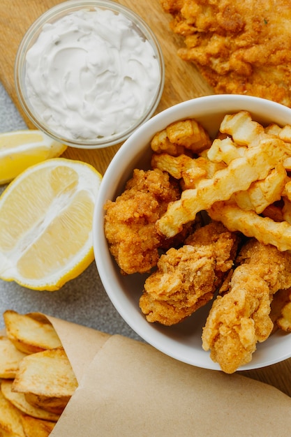 Flat lay of fish and chips in bowl and paper wrap with sauce