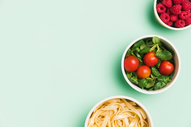 Flat lay food containers with raspberries, salad and pasta with\
copy-space