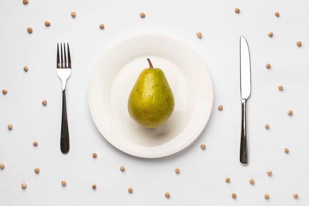 Flat lay of fresh pear on plate with cutlery