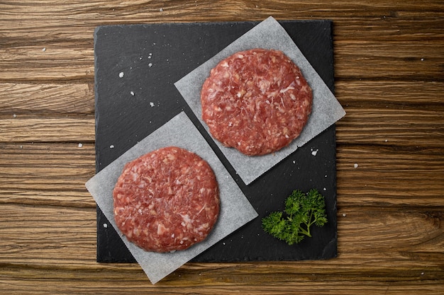 Flat lay of a fresh raw veal chop with herbs on a black kitchen board