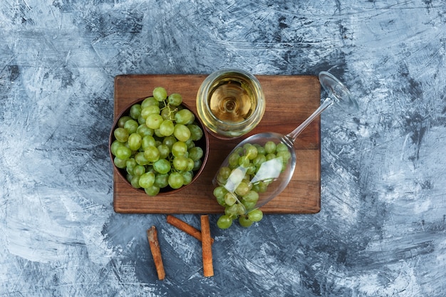 Foto gratuita piatto laici bicchiere di whisky, uva bianca sul tagliere con cannella su marmo blu scuro dello sfondo. orizzontale