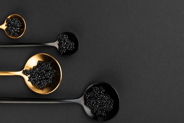 Flat lay of golden and black spoons with caviar