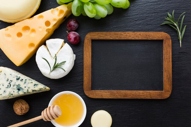 Flat lay gourmet cheese mix and honey with blank blackboard