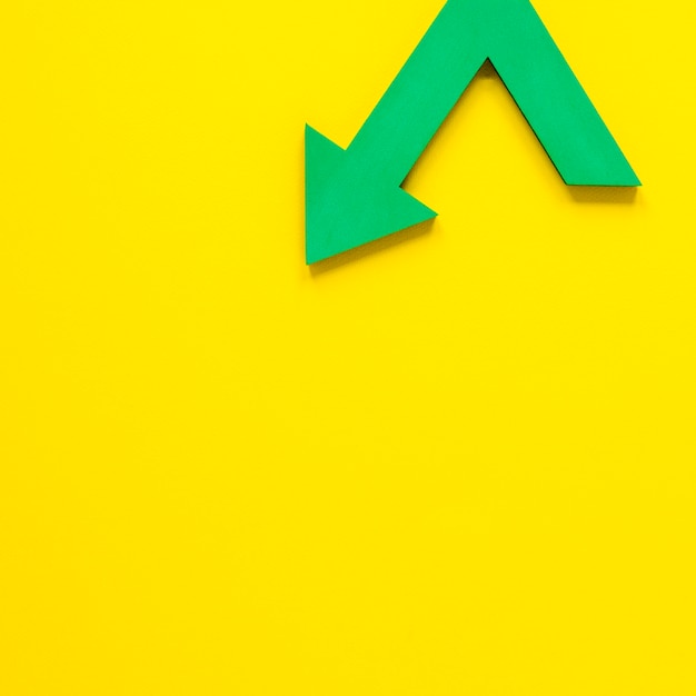 Flat lay green arrow on yellow backgroundwith copy-space