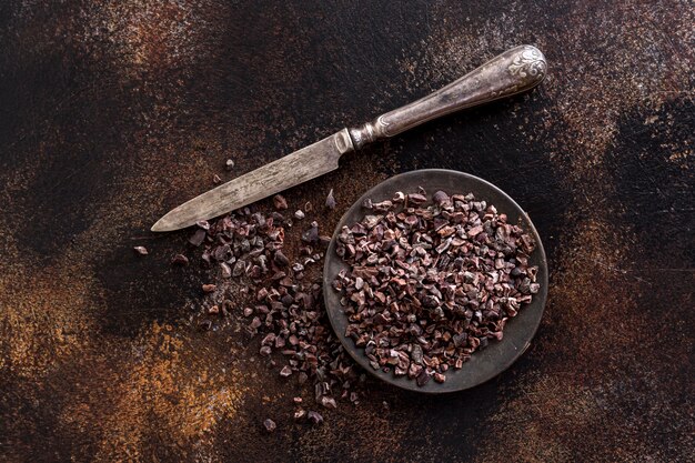Flat lay of grounded cocoa beans on plate with knife
