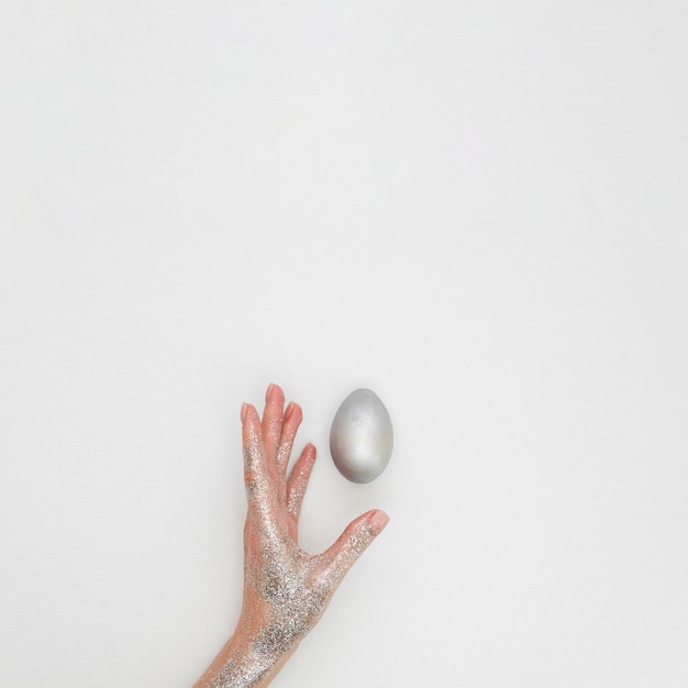 Free photo flat lay of hand covered in glitter with painted easter egg