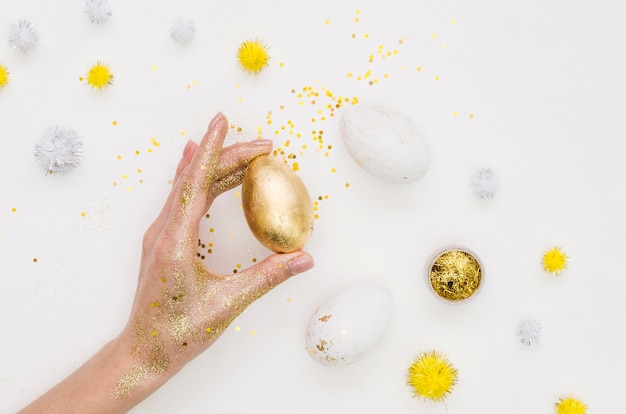 Flat lay of hand holding holding egg for easter with dandelions and glitter
