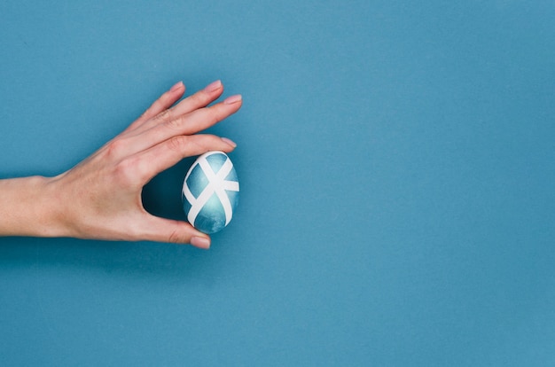 Flat lay of hand holding painted easter egg with copy space