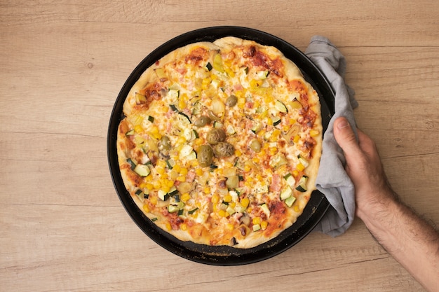 Flat lay hand holding pan with cooked pizza