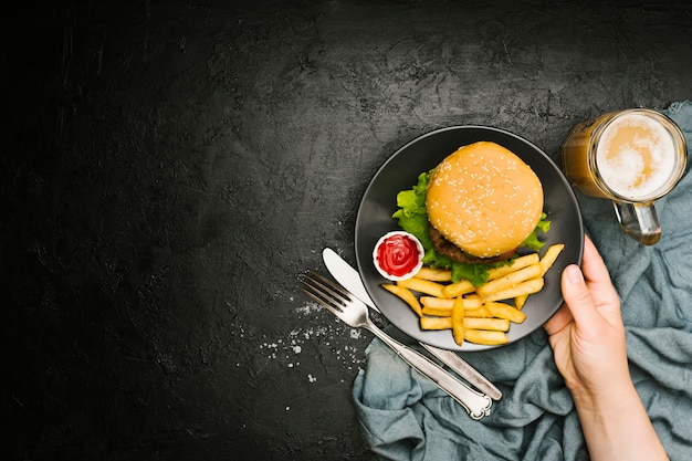 Flat-lay hand holding plate with burger and fries with copyspace