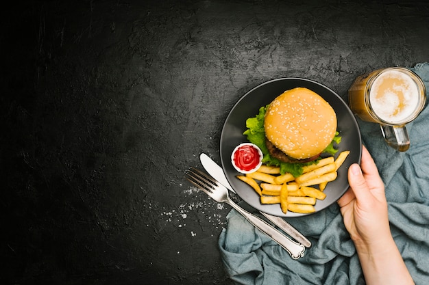 Плоская рука держит тарелку с гамбургером и картофелем фри с copyspace