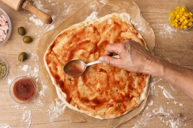 Flat lay hand spreading tomato sauce on pizza dough