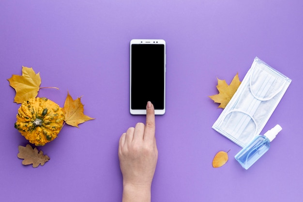 Flat lay of hand using smartphone with medical mask and autumn leaves