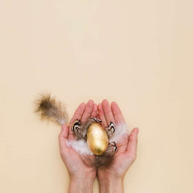 Flat lay of hands holding golden easter egg with feathers and copy space