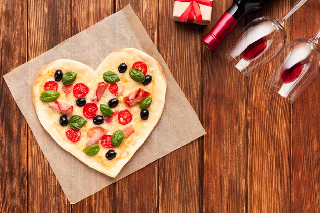 Flat lay heart shaped pizza with wine