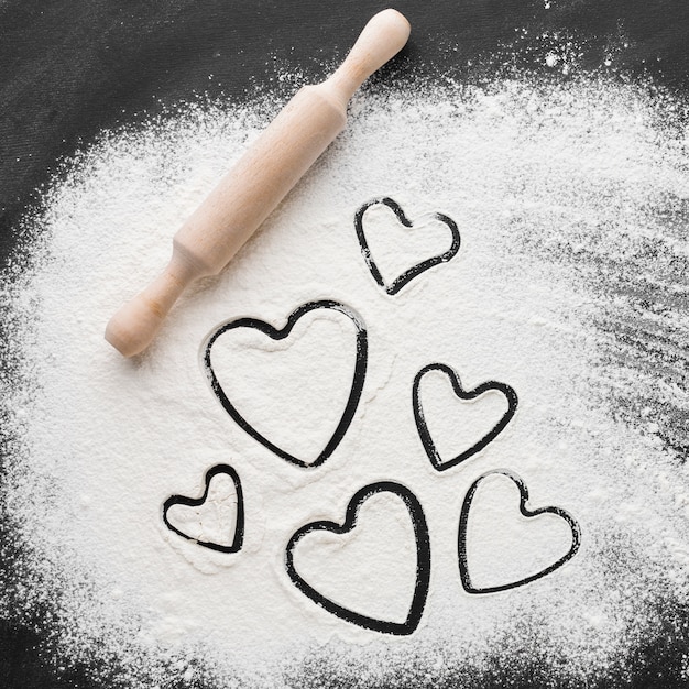 Free photo flat lay of heart shapes in flour with rolling pin