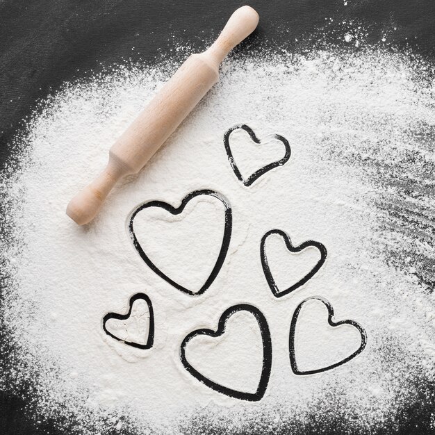 Flat lay of heart shapes in flour with rolling pin