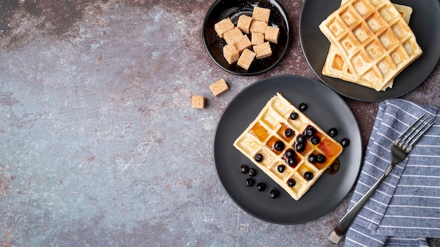 Flat lay of honey covered waffles on plate with fruits and copy space
