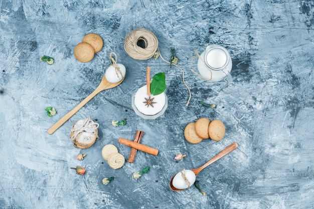 Flat lay a jug of milk and a glass bowl of yogurt with spoons,cookies,eggs,clew,cinnamon and a plant on dark blue marble surface. horizontal