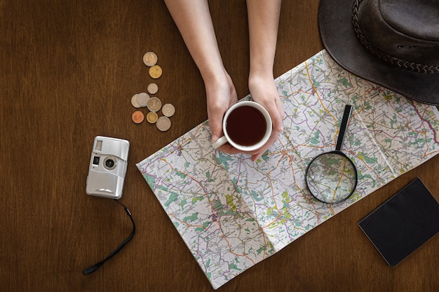 Flat lay, map, magnifier, documents and a cup of coffee in the hands of a woman.