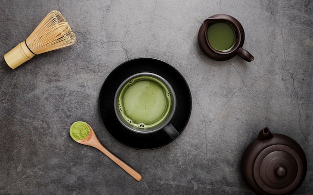 Flat lay of matcha tea in cup on plate with bamboo whisk