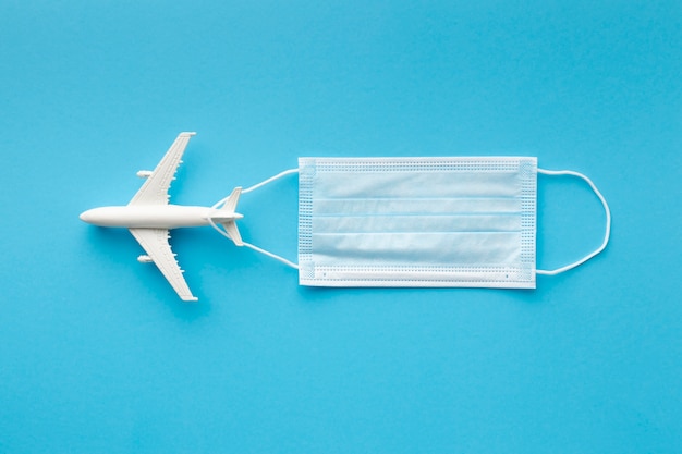 Flat lay of medical mask with airplane figurine