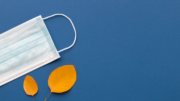 Flat lay of medical mask with autumn leaves and copy space