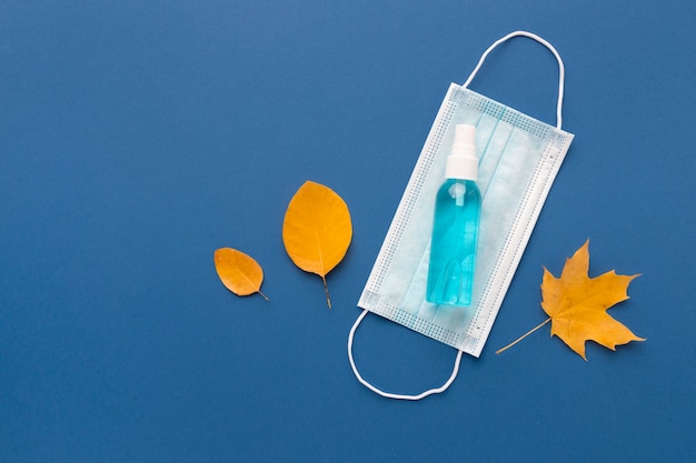 Flat lay of medical mask with hand sanitizer and autumn leaves