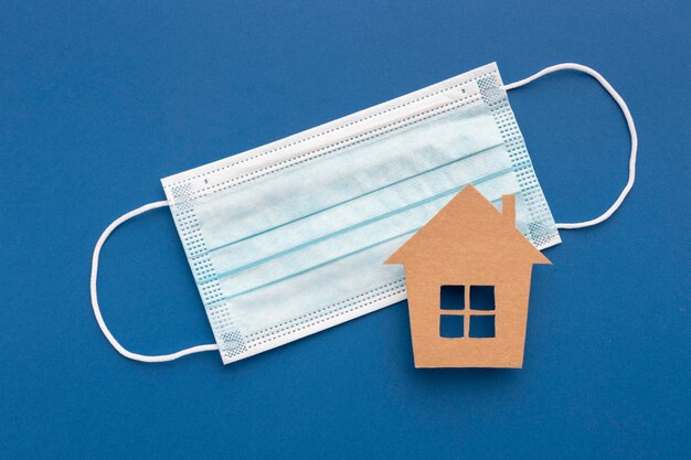 Flat lay of medical mask with house figurine