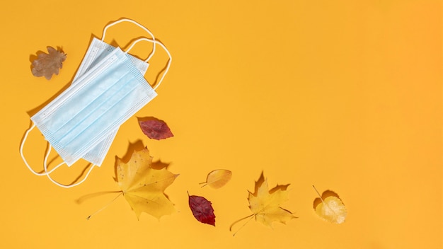 Flat lay of medical masks with autumn leaves and copy space