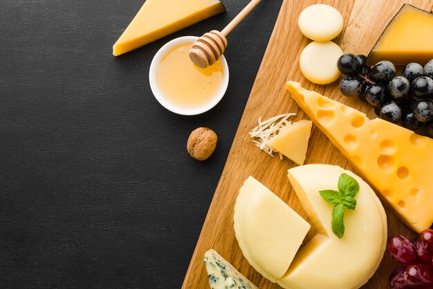 Flat lay mix of gourmet cheese and grapes on cutting board with honey