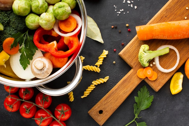 Free photo flat lay mix of vegetables and chicken drumstick in pan with carrot on cutting board