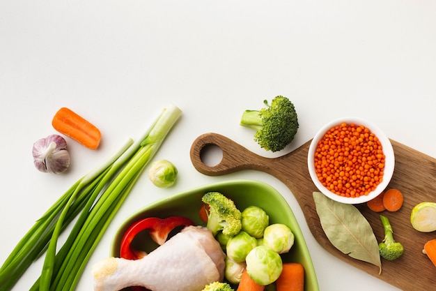 Free photo flat lay mix of vegetables on cutting board and in bowl with chicken drumstick and spoon